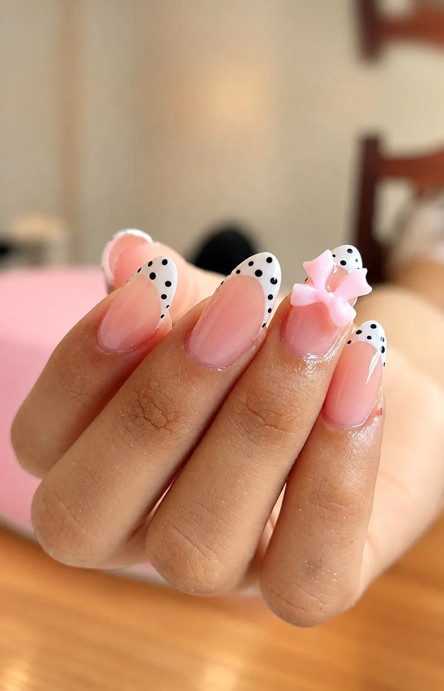 Uñas almendradas con francesa blanca de lunares negros y un lazo rosa en 3D