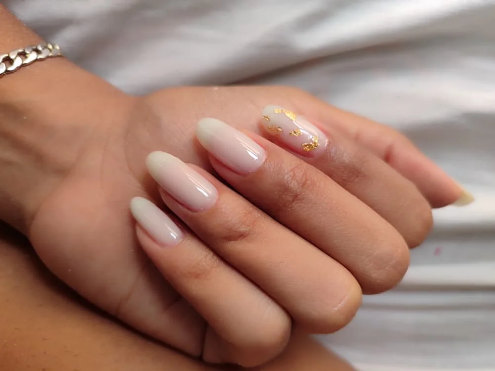 Uñas almendradas nude con detalle dorado sobre tela blanca