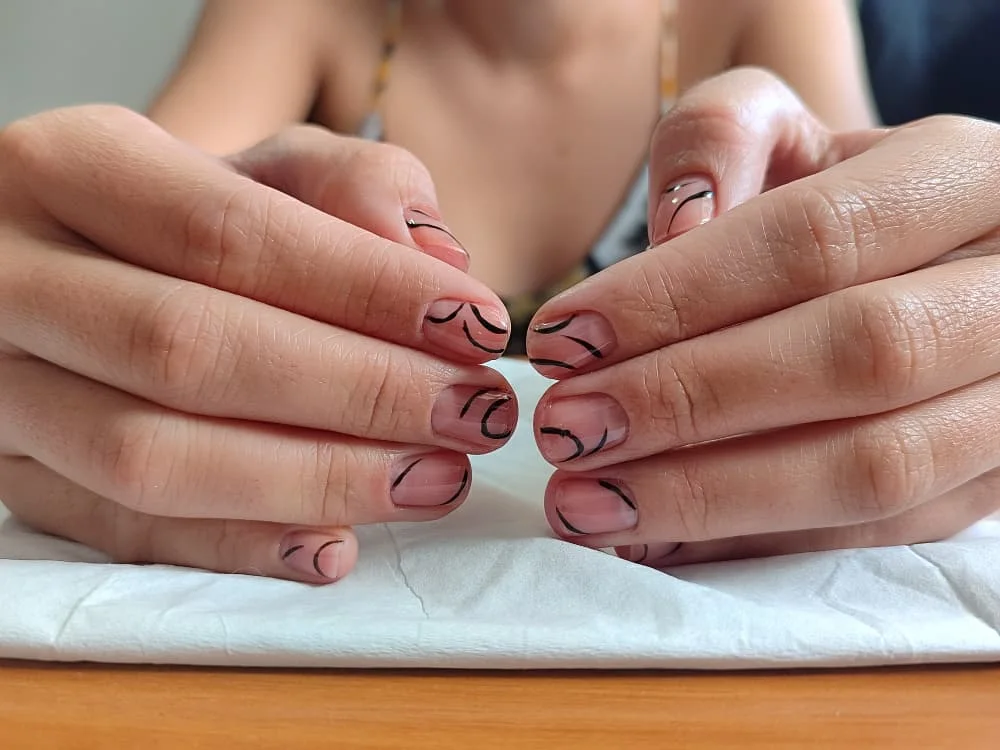 Uñas nude con trazos curvos negros y detalles rosas